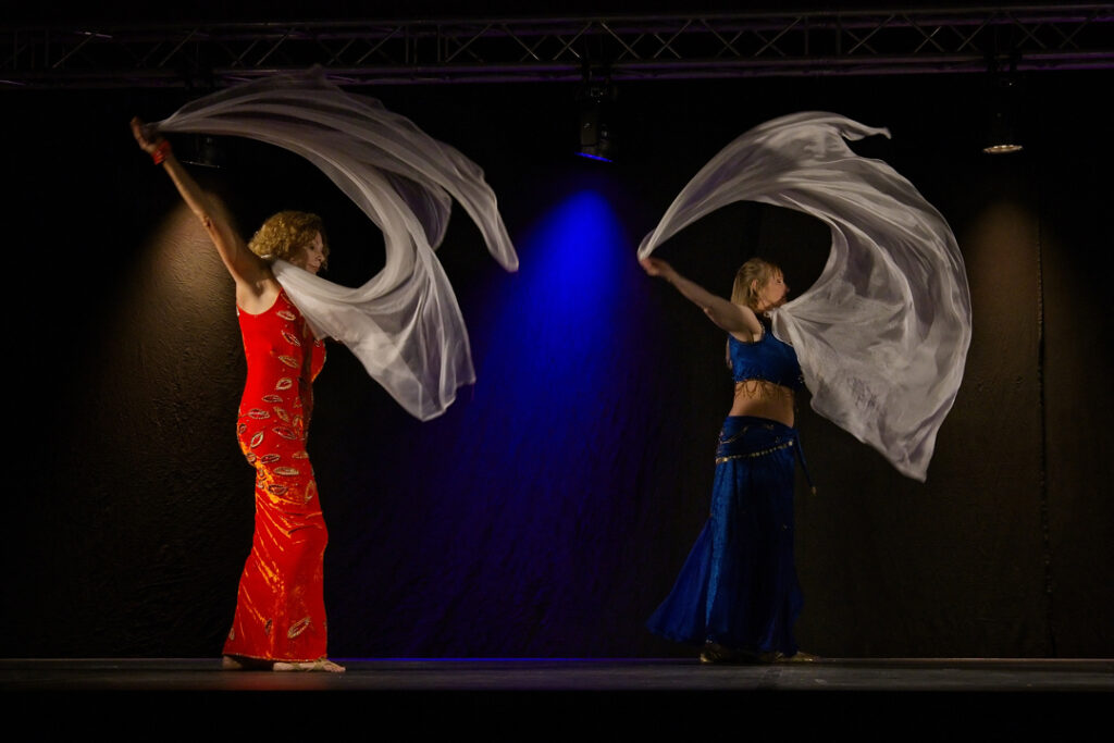 To elever fra optrædegruppen Nesrite optræder med slør under Oriental Festival Denmark i Kolding. Mørk baggrund fremhæver bevægelse og farver på slørene.