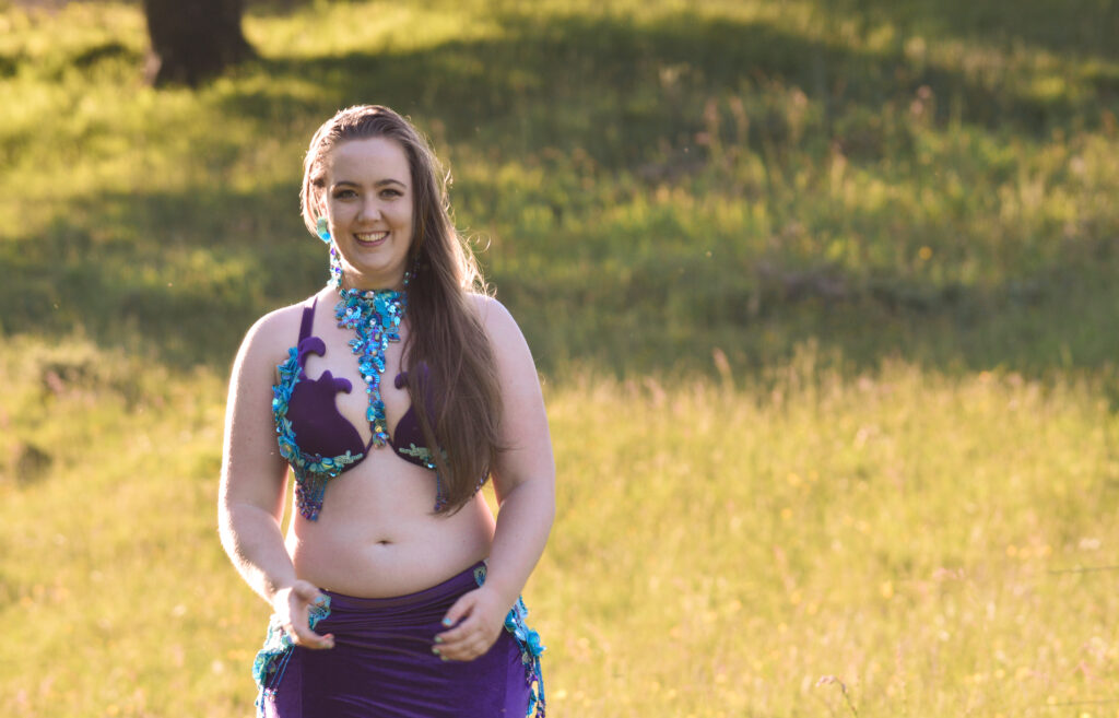 Amanda Salma står i grøn, frodig natur, smilende og imødekommende, klar til at undervise i mavedans.