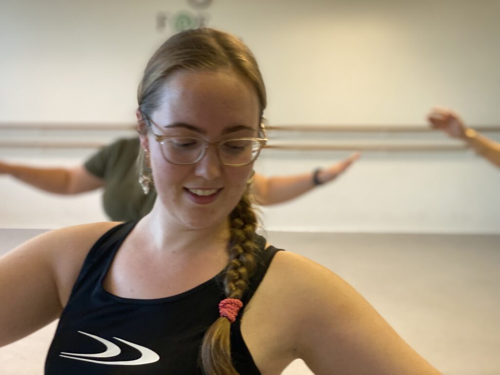 Close-up af Amanda Salma med et fokuseret og følsomt ansigtsudtryk under mavedansundervisning i Brostræde, Kolding. Eleverne træner i baggrunden, let sløret.