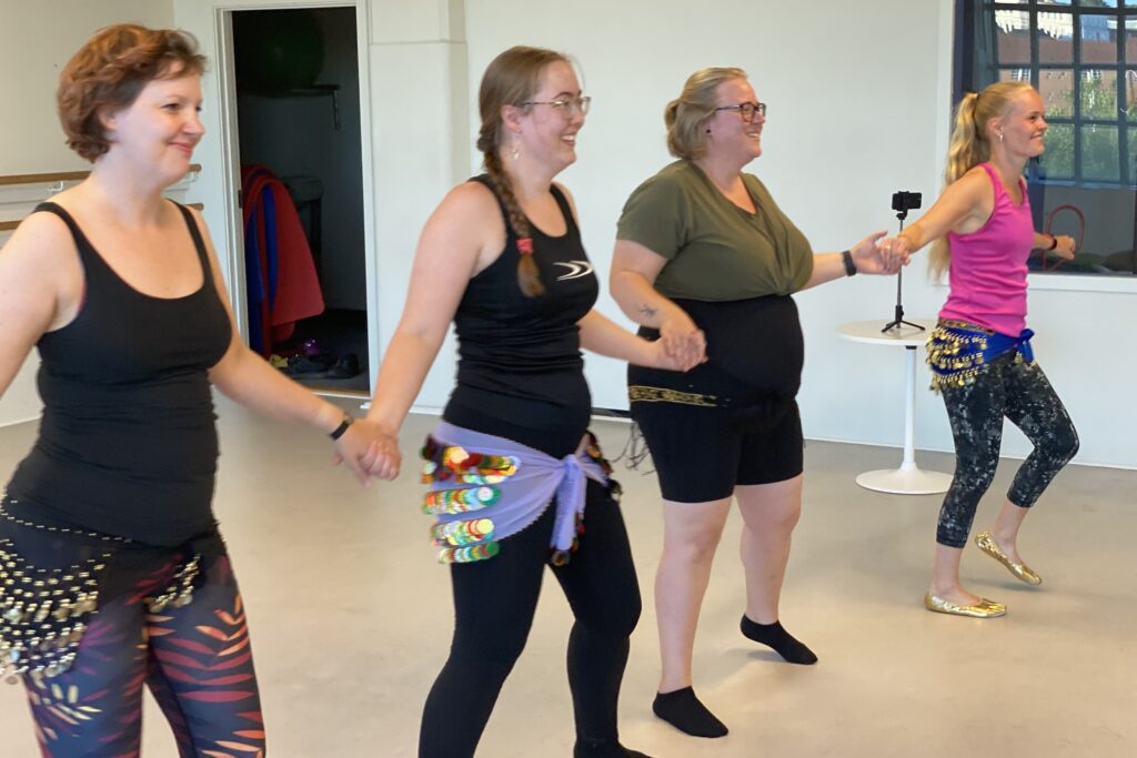 Amanda Salma underviser mavedans i Brostræde, Kolding. Hun og et par elever står i træningstøj og holder hinanden i hænderne.