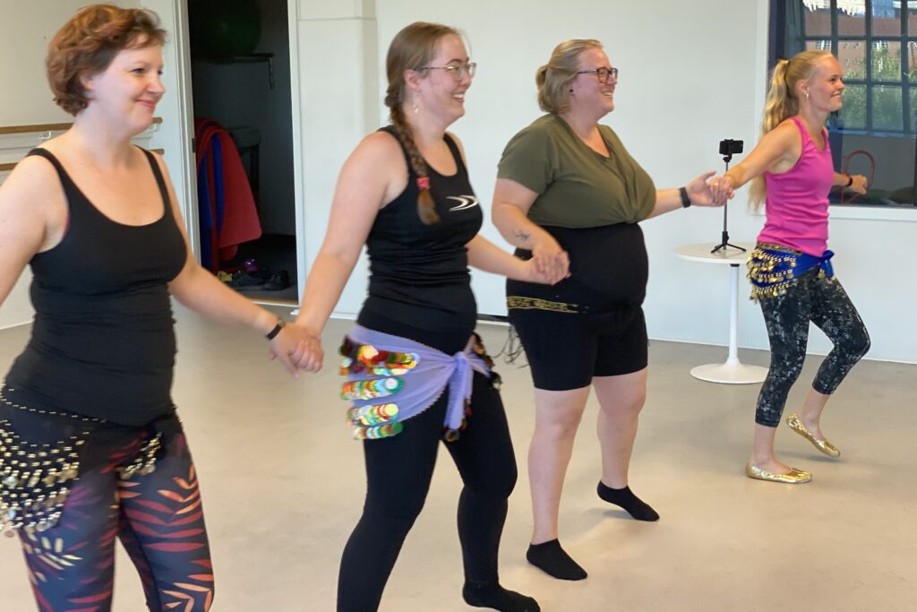 Amanda Salma underviser mavedans i Brostræde, Kolding. Hun og et par elever står i træningstøj og holder hinanden i hænderne.