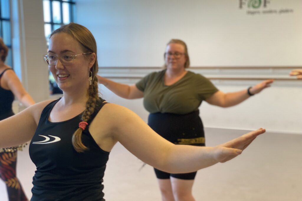 Amanda Salma underviser mavedans i Brostræde, Kolding. Hun står i træningstøj med et par elever bagved, mens de øver klassiske raqs sharqi-trin.